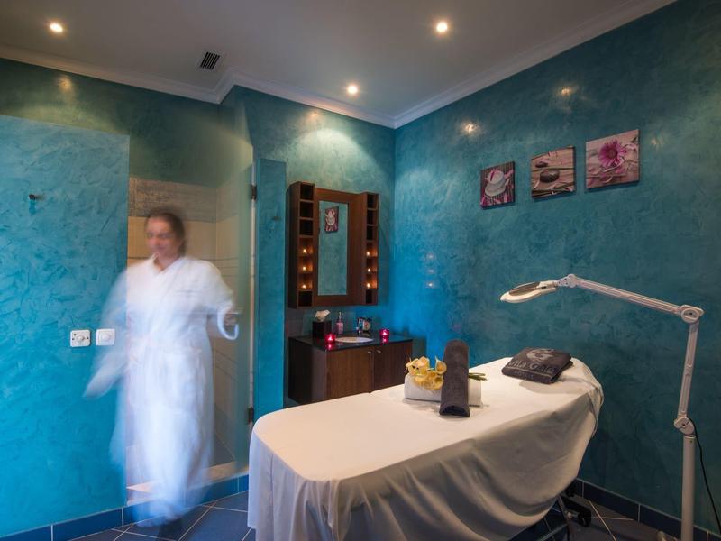 Behandlungsraum mit blau-grünen Wänden, Liege, Lampe und verschwommener Person im weißen Kittel.