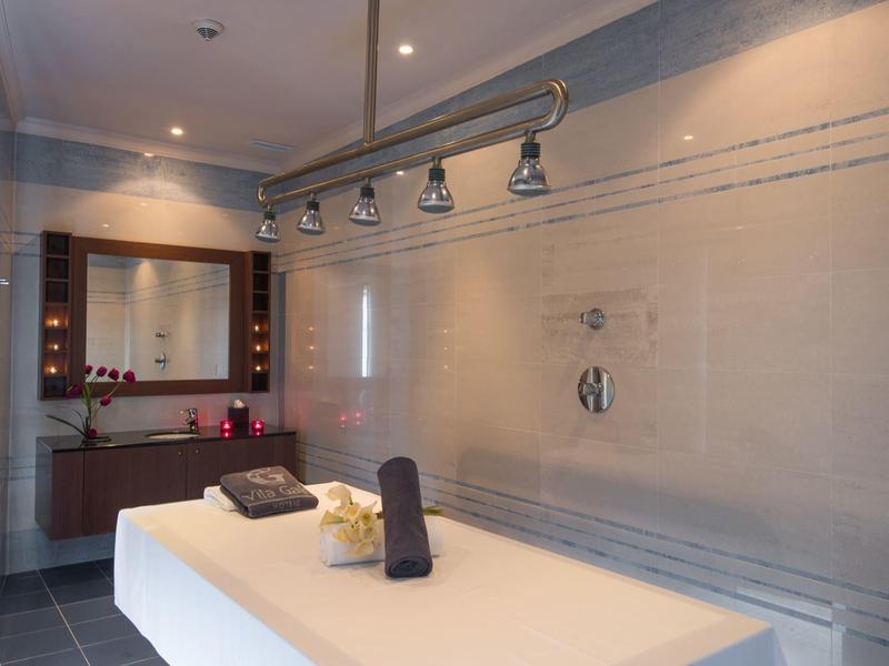 Moderner Wellnessraum mit Massagebank, Grauwänden, Spiegel, Handtüchern und indirektem Licht.