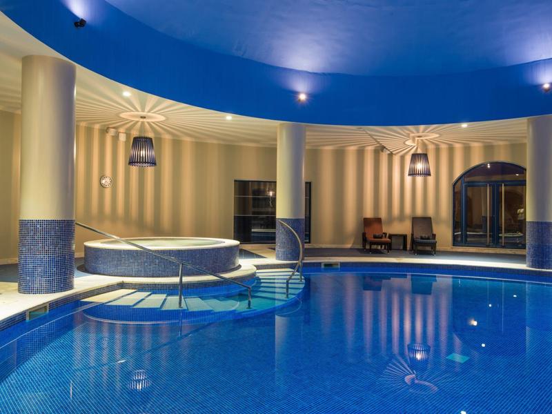 Runder, blauer Hallenpool mit integriertem Whirlpool, Säulen und abgerundetem blauen Deckendach.