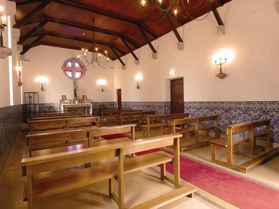 Innenraum einer kleinen Kirche mit Holzbänken, steinernen Wänden und einem Altar unter Holzbalken.