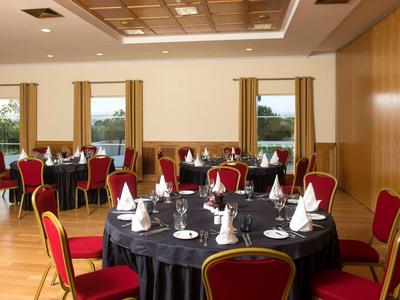 Ein heller Raum mit runden Tischen, schwarzen Tischdecken und roten Stühlen, gedeckt für ein Essen.