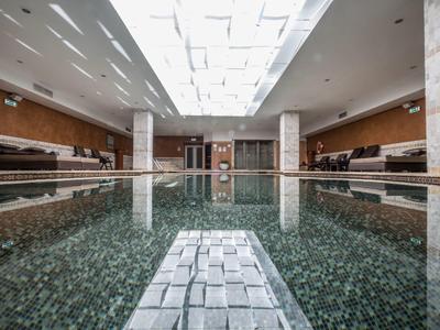 Großes Hallenbad mit ruhigem Wasser, weißen Wänden und Deckenfenstern für Tageslicht.