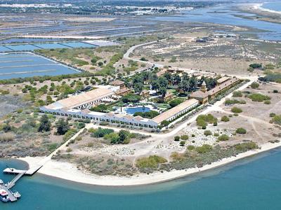 Insel mit Gebäuden, Sandstrand, Steg und umgeben von blauem Wasser und Feuchtgebieten.