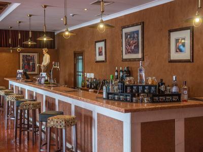 Elegante Bar mit langem Holztresen, Barhockern, warmen Wänden und dekorativen Bildern.