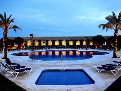 Beleuchteter Poolbereich mit Palmen, Liegestühlen und blauem Abendhimmel.