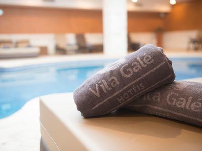 Zwei dunkelgraue Handtücher mit weißer Aufschrift liegen gefaltet am Beckenrand eines Hallenbads.