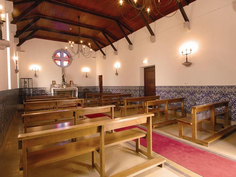 Innenraum einer kleinen Kirche mit Holzbänken, steinernen Wänden und einem Altar unter Holzbalken.