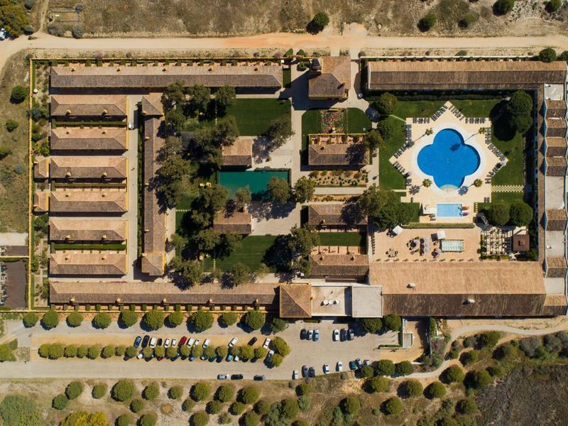 Großes Hotel mit mehreren Gebäuden, Pool in Blattform, Parkplätze und viele grüne Bäume.