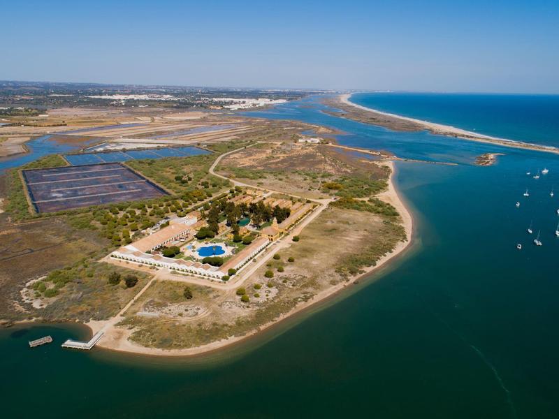 Luftaufnahme einer Landzunge mit Gebäuden, Solarzellen und Booten auf blauem Wasser.