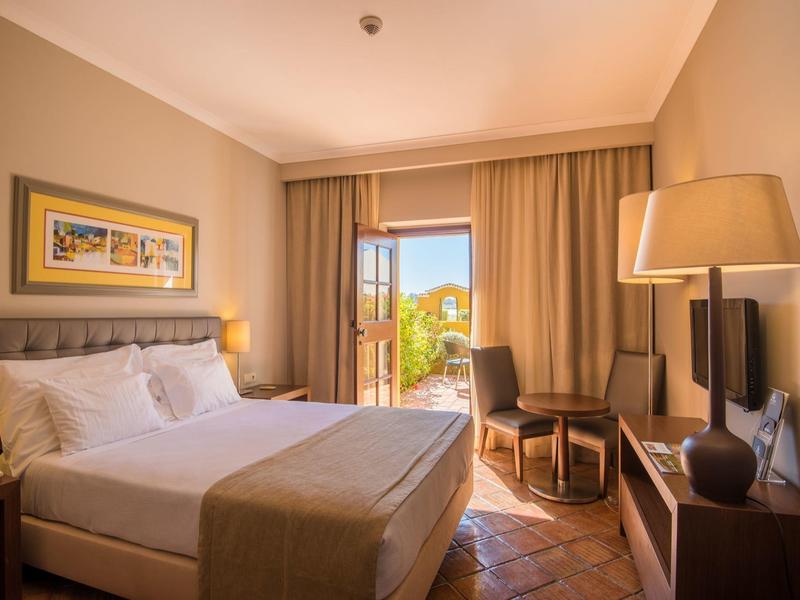 Gemütliches Schlafzimmer mit Doppelbett, Nachttischlampen, Sessel, TV und Balkon mit Naturblick.