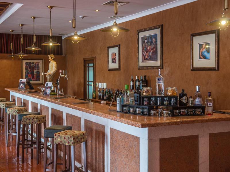 Elegante Bar mit langem Holztresen, Barhockern, warmen Wänden und dekorativen Bildern.