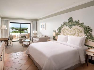 Helles Schlafzimmer mit großem Bett, verziertem Kopfteil, Fliesenboden und Terrasse mit Aussicht.