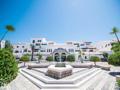 Complejo hotelero blanco moderno con piscina y palmeras bajo un cielo azul claro