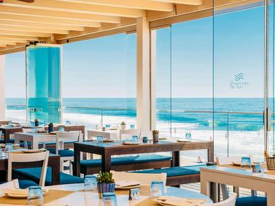 Helles Restaurant mit Meerblick und modernen Holzmöbeln an sonnigem Tag.