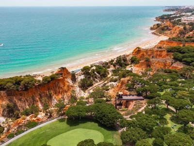 Küstenlandschaft mit Strand, klarem Wasser und grüner Vegetation neben einer Golfanlage.