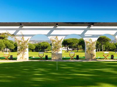 Jardín verde con columnas blancas, sillas colgantes y vista a colinas bajo cielo despejado.