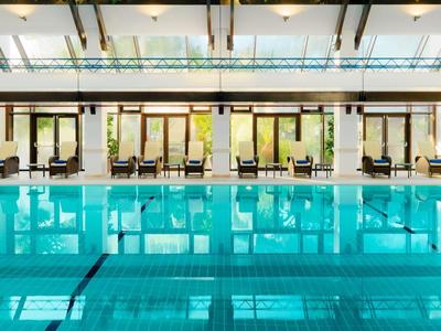 Ein klarer Innenpool in einem modernen Hotel mit Liegestühlen und Glaswänden.