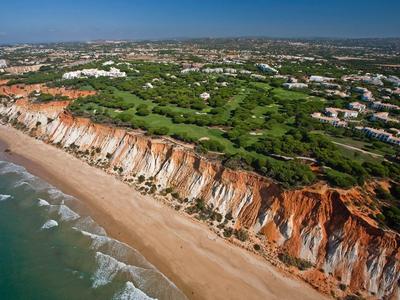 Roter Klippenstrand mit grünem Wald und blauer Meeresküste unter klarem Himmel.