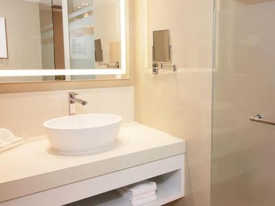 Helles Badezimmer mit modernem Waschbecken, Spiegel und Handtüchern auf offenem Regal.