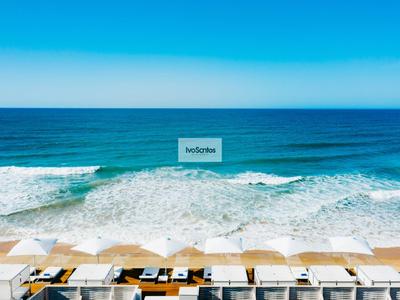 Blick auf einen Strand mit weißen Sonnenschirmen und blauer Meeresbrandung unter klarem Himmel.
