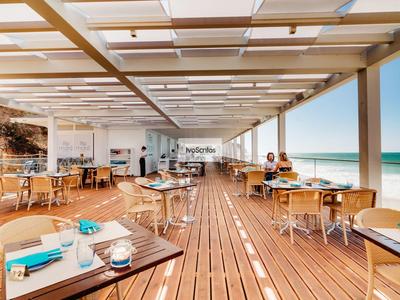 Offenes Strandrestaurant mit Holzboden und Tischen mit blauem Geschirr und Meerblick.