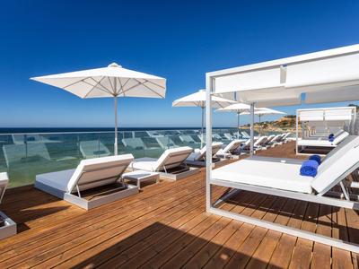 Entspannungsbereich mit Liegen und Sonnenschirmen auf Holzterrasse mit Meerblick.