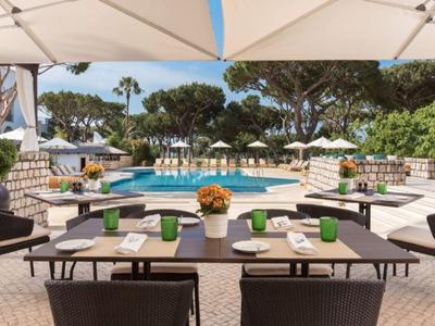 Moderner Außenbereich mit Tisch, Stühlen, Sonnenschirmen und Pool in grüner Umgebung.