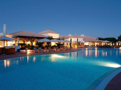 Abendaufnahme eines beleuchteten Hotelpools mit ruhigem Wasser und klar blauem Himmel.