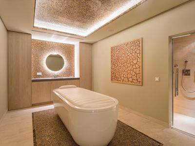 Modernes Badezimmer mit freistehender Badewanne, indirekter Beleuchtung und beiger Wanddekoration.