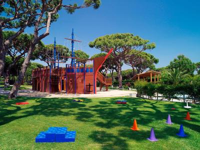Kinderspielplatz mit Piratenschiff und bunten Hütchen auf grünem Rasen unter blauem Himmel.