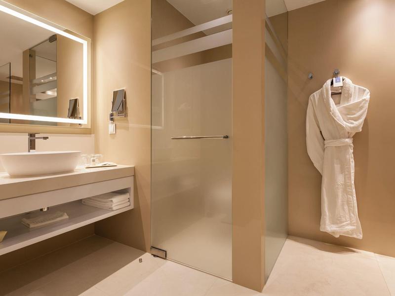 Modernes Hotelbadezimmer mit Glasdusche und Bademantel an der Wand.