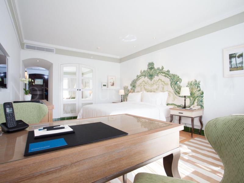 Helles, geschmackvoll eingerichtetes Schlafzimmer mit grünem Kopfteil, Schreibtisch und weißen Wänden.