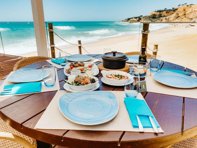 Tisch mit Tellern, Gläsern und Speisen am Strand mit Blick auf das Meer.
