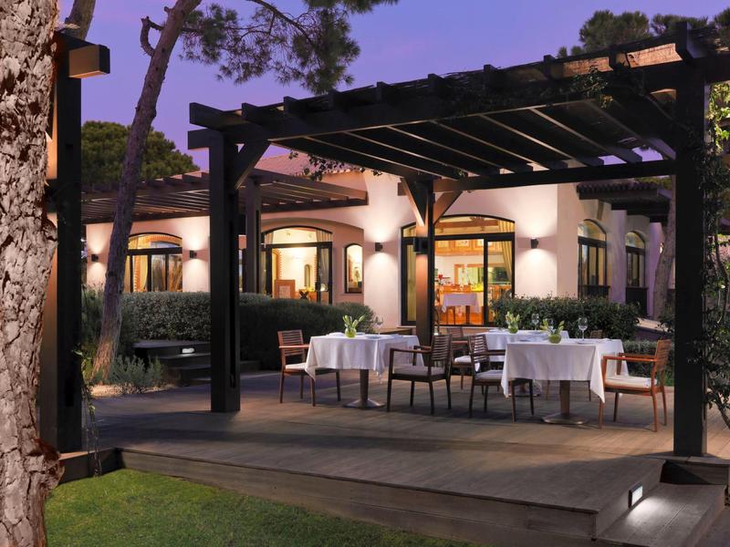 Außenbereich eines Restaurants mit weißen gedeckten Tischen unter einer Pergola bei Dämmerung.