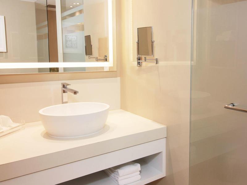 Helles Badezimmer mit modernem Waschbecken, Spiegel und Handtüchern auf offenem Regal.