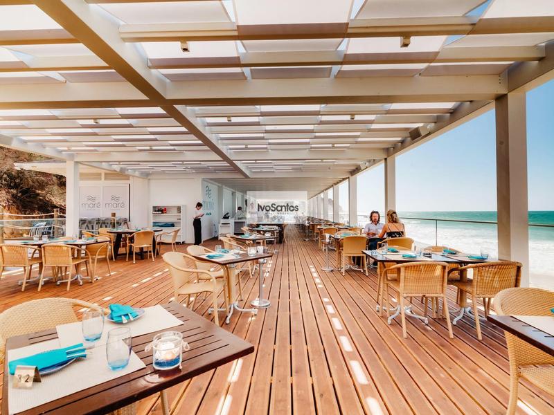 Offenes Strandrestaurant mit Holzboden und Tischen mit blauem Geschirr und Meerblick.