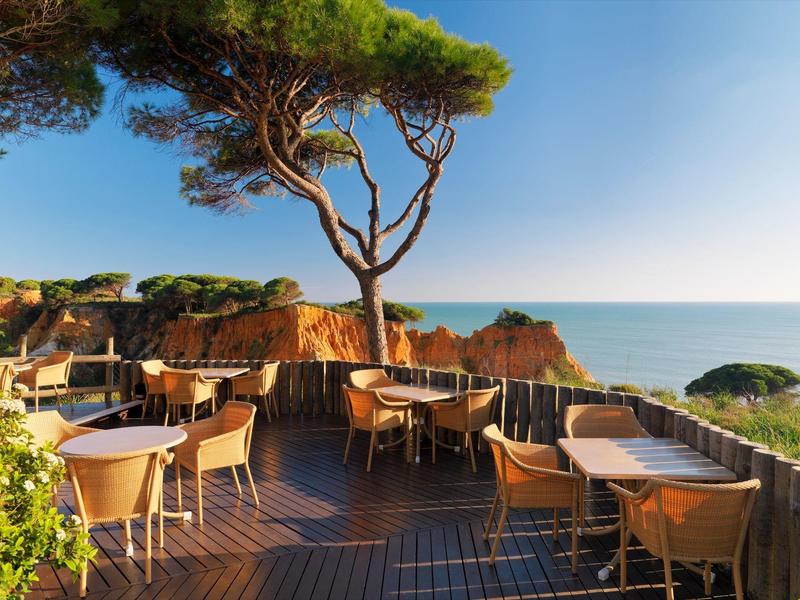 Terrasse mit Stühlen und Tischen mit Blick auf das Meer bei klarem Himmel.