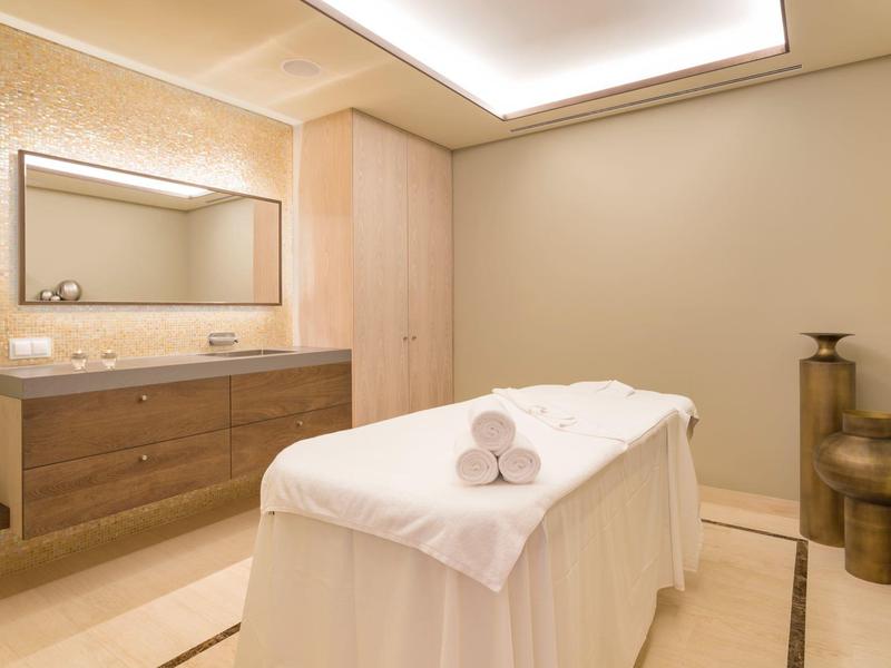 Helles Wellnesszimmer mit Massagebank, Handtüchern, Spiegel und schlichter Dekoration.