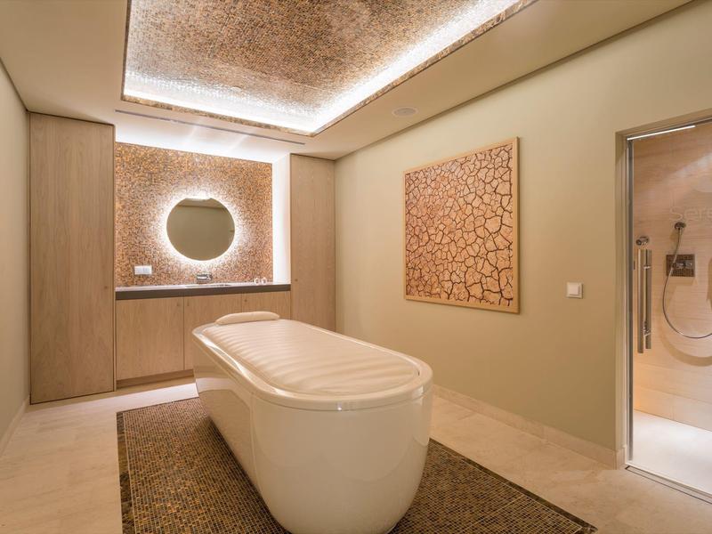 Modernes Badezimmer mit freistehender Badewanne, indirekter Beleuchtung und beiger Wanddekoration.