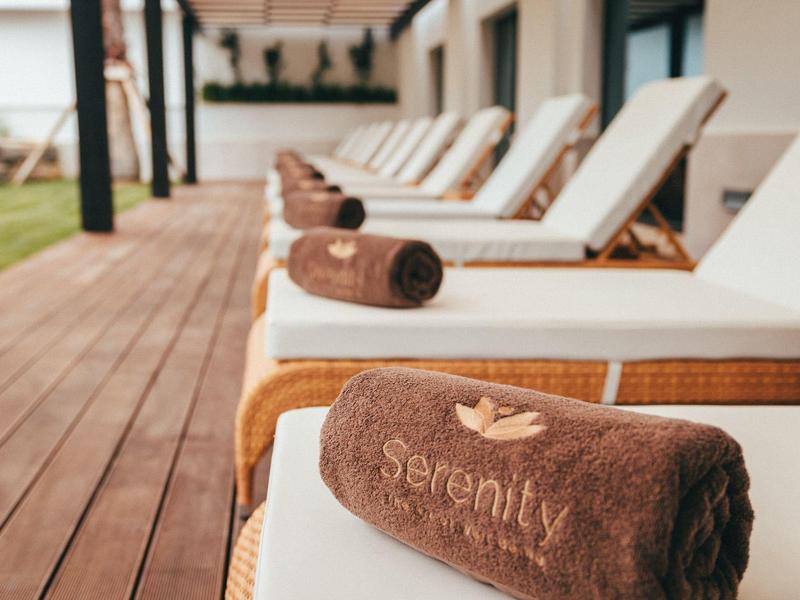 Mehrere Liegestühle mit braunen Handtüchern an einem hölzernen Pooldeck.