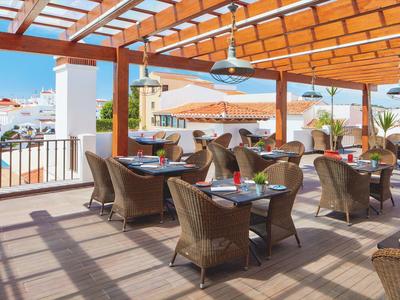 Offener Gartenbereich mit Korbsesseln, Tischen und Pergola-Dach bei Sonnenschein.