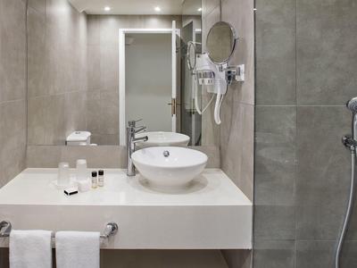 Modernes Bad mit weißem Waschbecken, großem Spiegel, grauen Fliesen und klarer, minimalistischer Gestaltung.