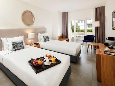 Hotelzimmer mit zwei Einzelbetten, modernem Holzmobiliar und Zugang zu einem Balkon.