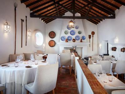 Elegantes Restaurant mit weißen Tischen, bequemen Stühlen und Holzbalkendecke, dekorative Teller an der Wand.