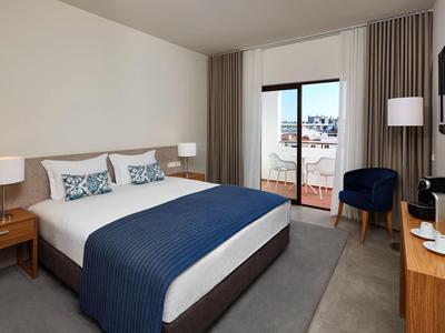 Modernes Schlafzimmer mit großem Bett, blauen Akzenten, Balkon und stilvollen Möbeln in neutralen Farben.