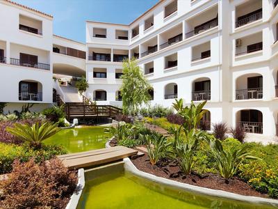 Innenhof eines weißen Wohngebäudes mit mehreren Etagen, grünen Pflanzen und einem kleinen Teich.