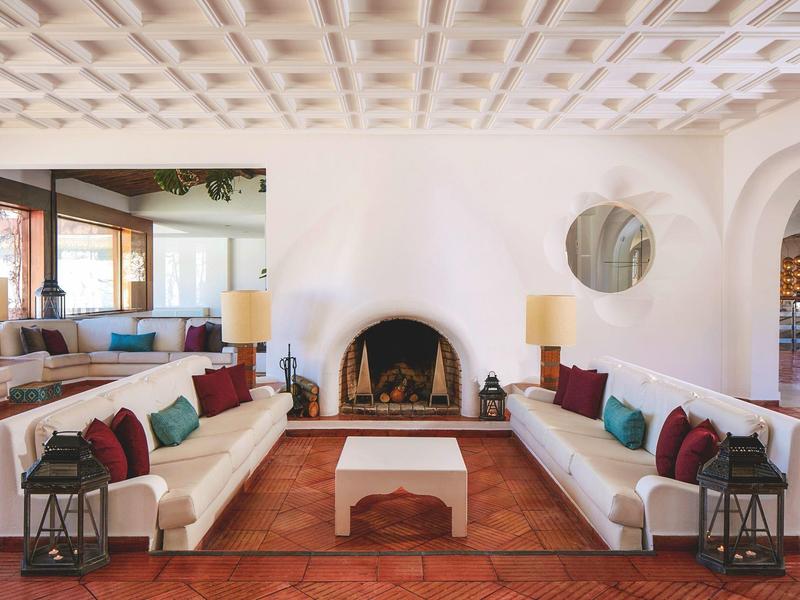 Heller Wohnraum mit weißen Sofas, bunten Kissen, rundem Kamin und Terrakottaboden.