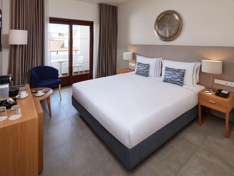 Modernes Schlafzimmer mit großem Doppelbett, dunkelblauen Sesseln und Holzmöbeln, hell und gemütlich.