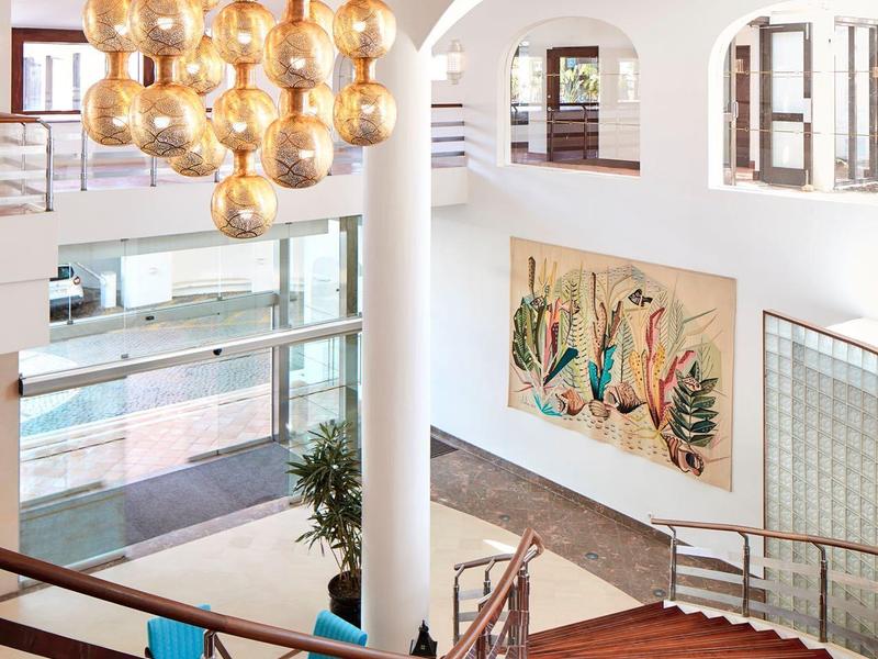 Modernes Treppenhaus mit Holzstufen, weißen Wänden, großen Fenstern und goldglänzender Kugelleuchte.