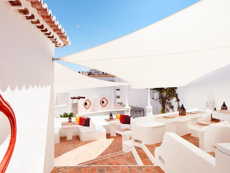 Gemütliche weiße Terrasse mit rot-weißer Dekoration und offenem blauen Himmel.